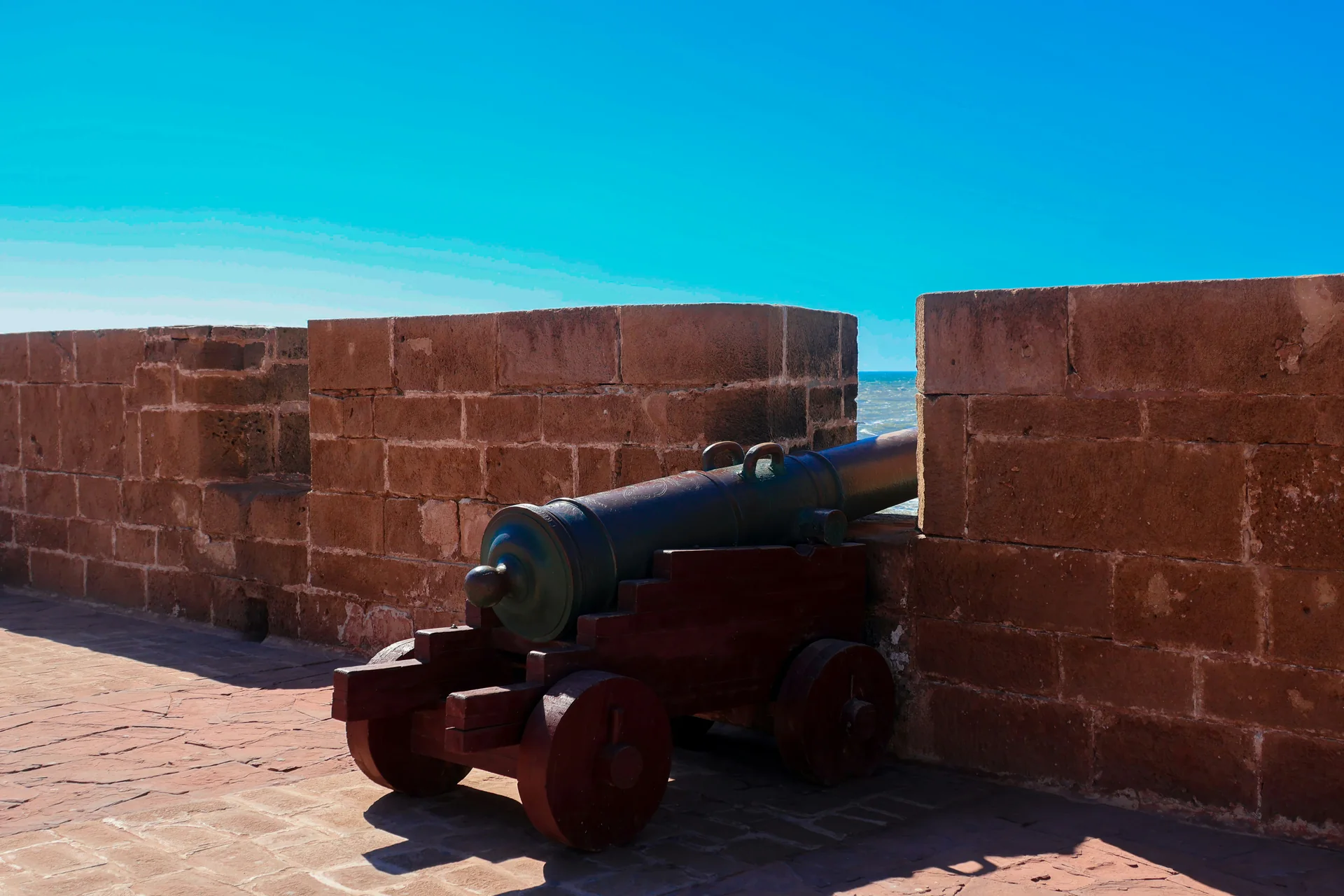 An 18th-century cannon mounted on the Skala de la Ville sea rampart in Essaouira, Morocco, the Atlantic visible through the sandstone battlements