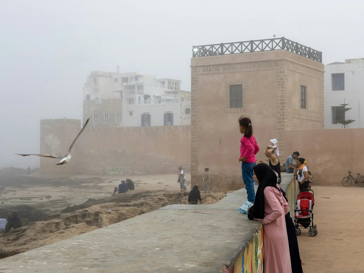 Essaouira's sea-wall promenade in coastal fog, the medina's white and ochre buildings behind